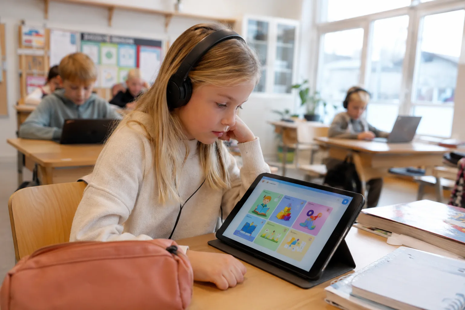 Elev som sitter ved en pult med et nettbrett og hodetelefoner i et norsk klasserom