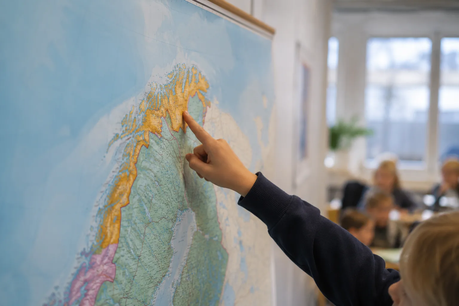 Nærbilde av en pekefinger som peker på Troms og Finnmark fylke på et skolekart